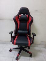 Ergonomic red and black racing-style gaming chair with headrest and lumbar pillows, featuring a high backrest and adjustable armrests on a sturdy five-star base.
