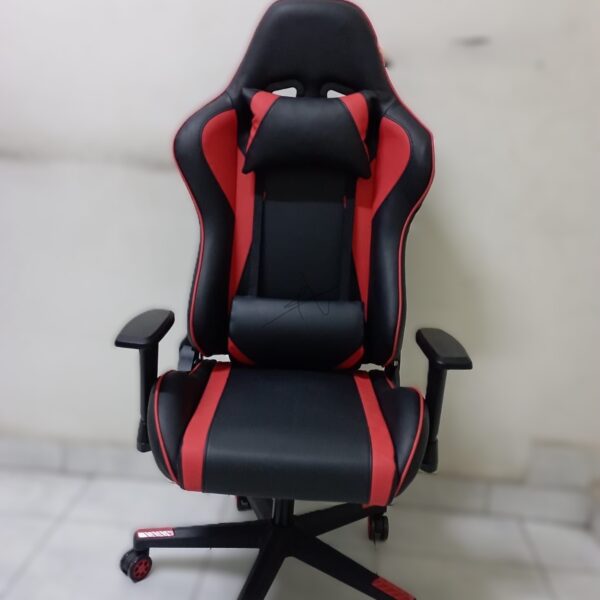 Ergonomic red and black racing-style gaming chair with headrest and lumbar pillows, featuring a high backrest and adjustable armrests on a sturdy five-star base.