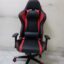 Ergonomic red and black racing-style gaming chair with headrest and lumbar pillows, featuring a high backrest and adjustable armrests on a sturdy five-star base.