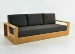 Modern executive lounge sofa with a thick solid oak frame and charcoal grey cushions shown from a perspective angle.