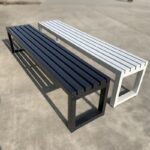 Durable black slatted metal backless bench with floor-mounting legs for commercial waiting rooms, hospitals, and outdoor public spaces.