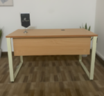 Modern wooden office desk with a light oak finish top, white metal U-shaped legs, and a matching wooden modesty panel, viewed from a high-angle perspective in a bright office setting.
