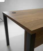Modern office desk with light oak wooden top, grey metal legs, modesty panel, and a built-in cable grommet on a tiled floor.
